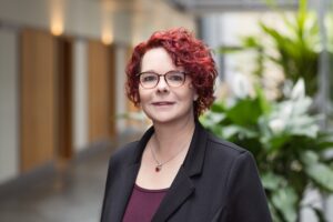 Mitarbeiterin der GfG mit Brille und schwarzem Blazer im hellen Flur
