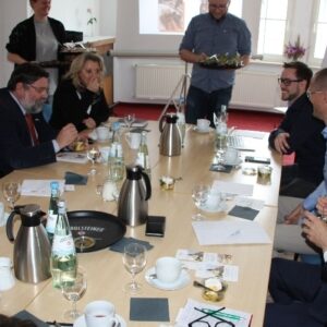 Mehrere Personen sitzen bei einer Besprechung an einem gedeckten Konferenztisch – Austausch und Vernetzung der GfG