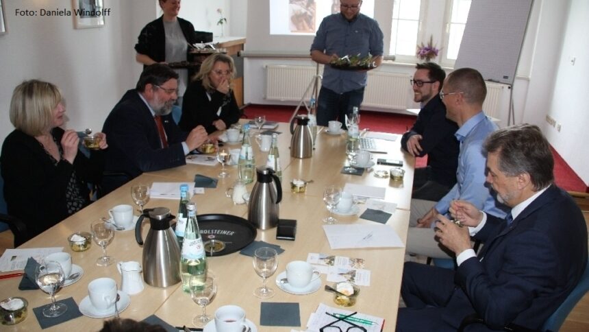 Mehrere Personen sitzen bei einer Besprechung an einem gedeckten Konferenztisch – Austausch und Vernetzung der GfG