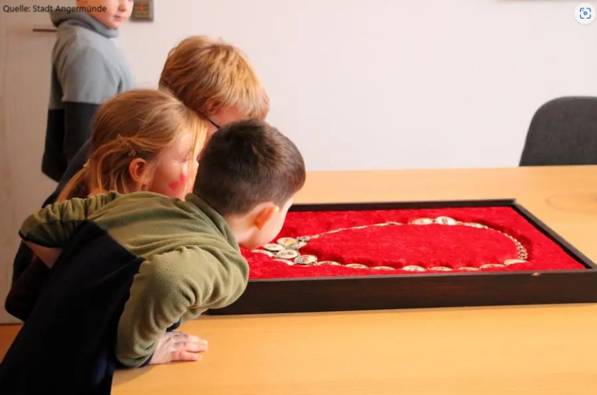 Drei Kinder betrachten neugierig eine Amtskette in einer roten Schaukassette
