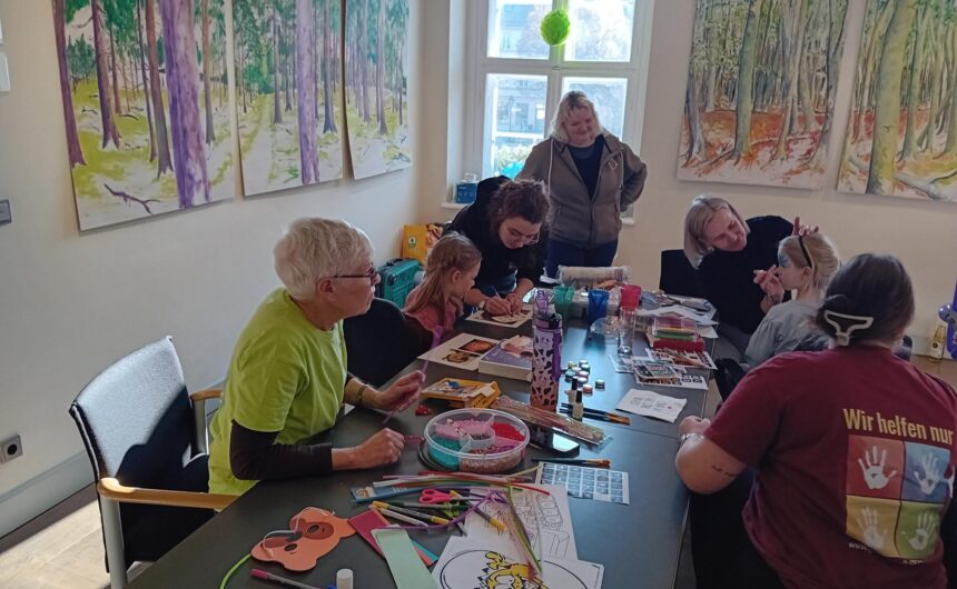 shared image (1) Kinder und Mitarbeitende der GfG bei einer Bastel- und Schminkaktion, im Hintergrund großformatige Waldbilder