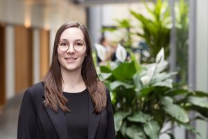 Mitarbeiterin der GfG mit Brille und schwarzem Blazer im hellen Flur