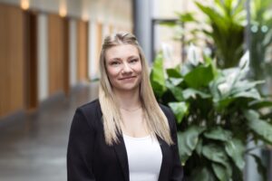 Blonde Mitarbeiterin der GfG mit schwarzem Blazer im hellen Flur