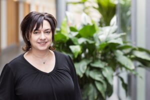 Mitarbeiterin der GfG mit dunklen Haaren und schwarzem Oberteil im hellen Flur